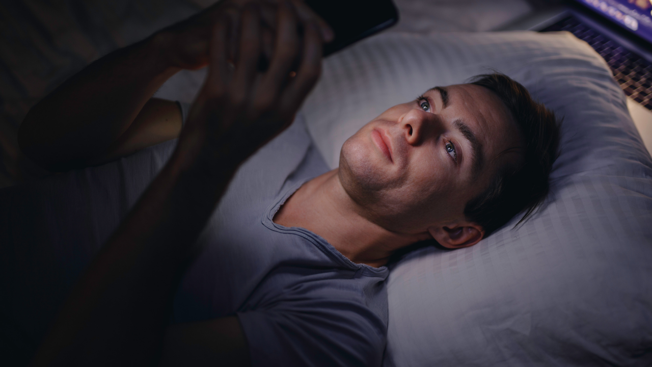 man staring at ceiling with eyes open in bed