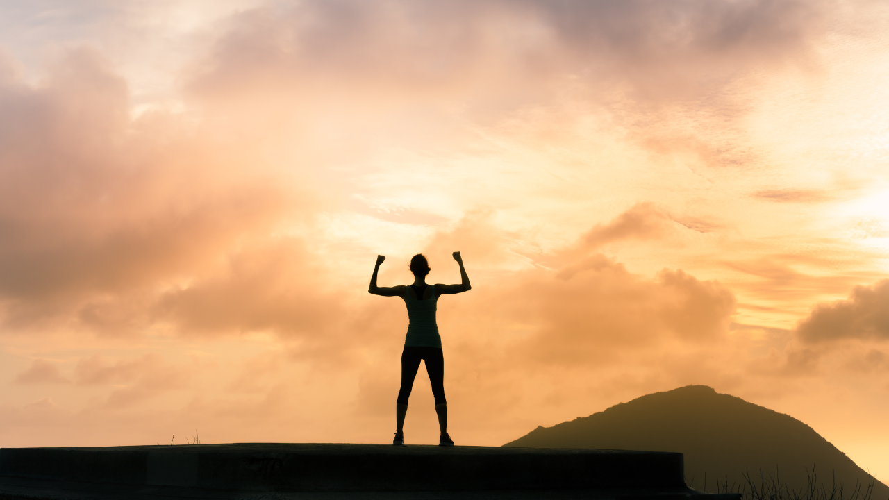 person with arms raised reaching top of a hill with setting sun