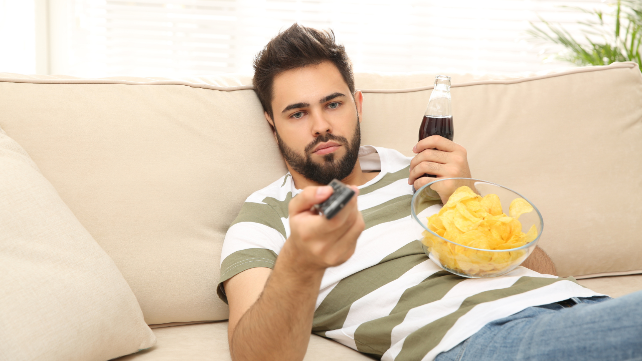 man sitting on couch with pop and chips